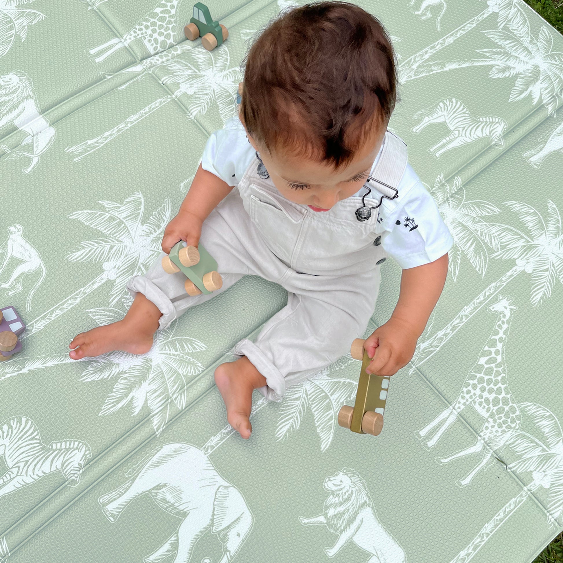 Baby playing on a green mat with animal patterns